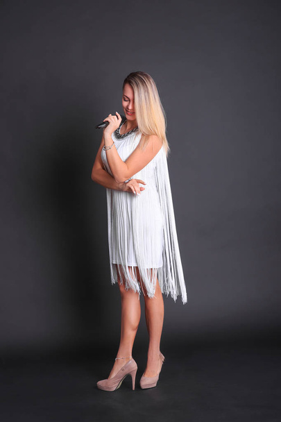 Girl with a microphone in a white dress in a photo studio on a black background - Fotó, kép