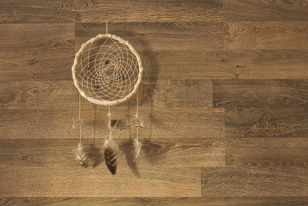 Atrapasueños con hilos de plumas y cuerda de cuentas colgando sobre fondo de pared de madera
 - Foto, Imagen