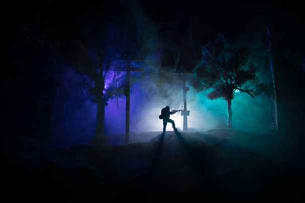Army sniper with large caliber rifle standing in the fire and smoke. War Concept. Battle scene on war fog sky background, Fighting silhouettes Below Cloudy Skyline at night. City destroyed by war - Photo, Image