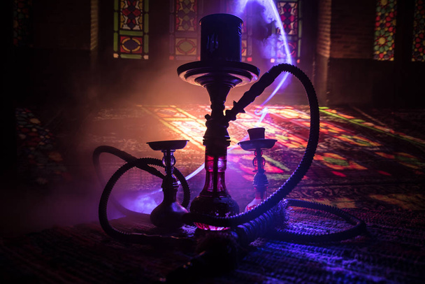 Hakka glühende Kohlen auf Shisha-Schüssel machen Dampfwolken im arabischen Inneren. Orientalische Ornamente auf dem Teppich. Stilvolle orientalische Shisha im Dunkeln mit Hintergrundbeleuchtung. - Foto, Bild