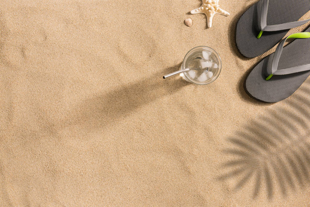 Top view of sandy beach with towel frame and summer accessories. Background with copy space and visible sand texture. Harsh light with shadows. - 写真・画像