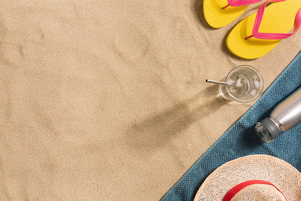 Summer vacation composition. Flip flops, water bottle and straw hat on sand background. Harsh light with shadows. Summer background. Border composition made of towel - Fotoğraf, Görsel