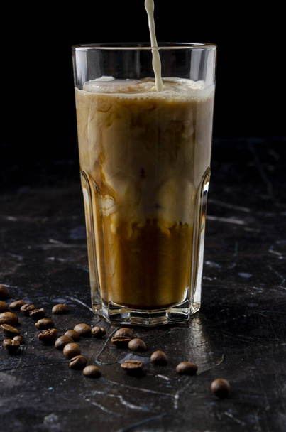 Iced coffee in a glass with pouring milk in black background - Foto, Imagem