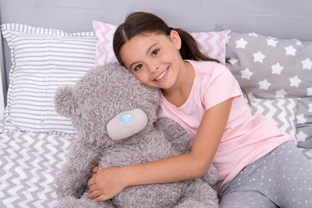 Kids evening routines. Favorite toy. Girl child hug teddy bear in her bedroom. Pleasant time in cozy bedroom. Girl kid long hair cute pajamas relax and play plush teddy bear toy. Pure love concept. - Photo, Image