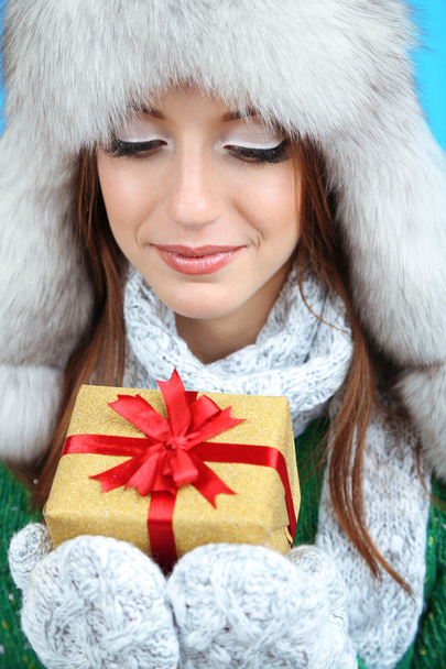 Beautiful smiling girl in hat with gift on blue background - Фото, изображение