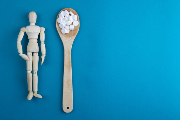 Wooden toy figure with pills on blue background. Various capsules, tablets and medicine on blue pastel trendy background. Pills concept. - 写真・画像