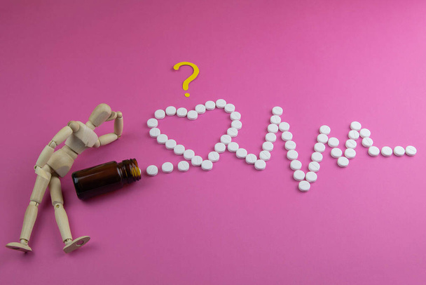 Figura giocattolo in legno con pillole a forma di cuore con cardiogramma su sfondo rosa. Concetto di pillole
. - Foto, immagini