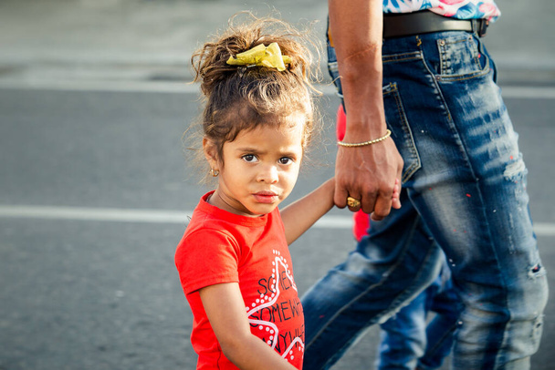 Concepcion De La Vega, DOMINICAN REPUBLIC - FEBRUARY 09, 2020: closeup portrait of small girl in bright clothes passes with parents by city street on February 9 in Concepcion De La Vega - Photo, Image