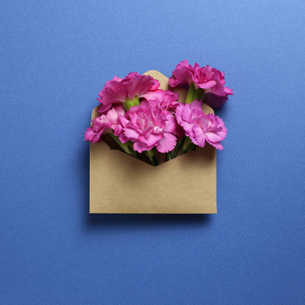 Pink spray carnation flowers in kraft envelope on dark blue background. Floral composition, flat lay, top view, copy space - Photo, Image