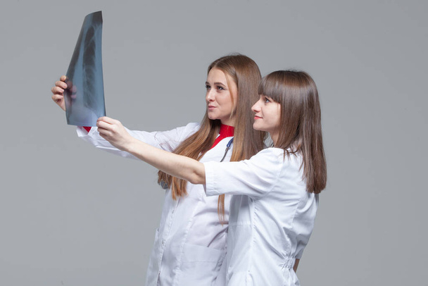 Two young female doctors looking at the x-ray picture of lungs on grey background - Photo, Image