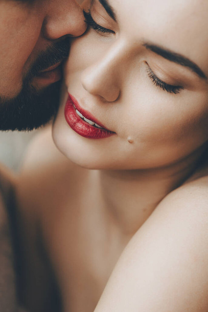 Εκπληκτική καυκάσιος κορίτσι με κόκκινα χείλη φιλείται από γενειοφόρος εραστής της, ενώ αγκαλιάζει ο ένας τον άλλον - Φωτογραφία, εικόνα