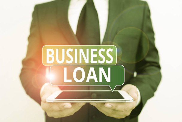 Conceptual hand writing showing Business Loan. Business photo showcasing Loans provided to small businesses for various purposes Male human wear formal work suit hold hitech smartphone. - Photo, Image