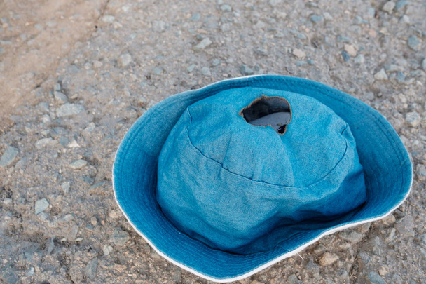 синяя летняя шляпа лежит на асфальте со следами пожара в центре. загорелась от жары летом шутка - Фото, изображение