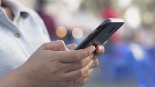 Mãos de mulher mensagem de texto no telefone inteligente móvel para comunicação e bate-papo no social on-line no mercado de comida de rua à noite. Iluminação bokeh fundo
. - Filmagem, Vídeo