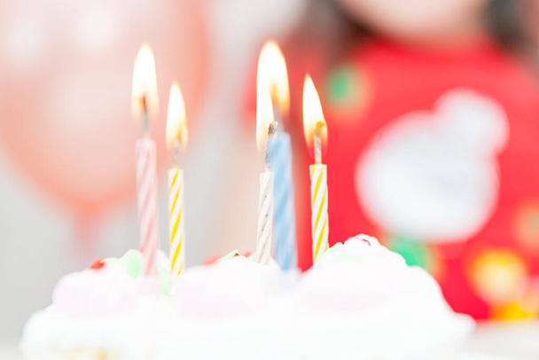 Sweet white birthday cake with candles and defocused happy little girl on the background during party celebration - 写真・画像