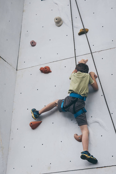Ένα μικρό αγόρι σκαρφαλώνει σε έναν πέτρινο τοίχο. Έννοια της αθλητικής ζωής. - Φωτογραφία, εικόνα