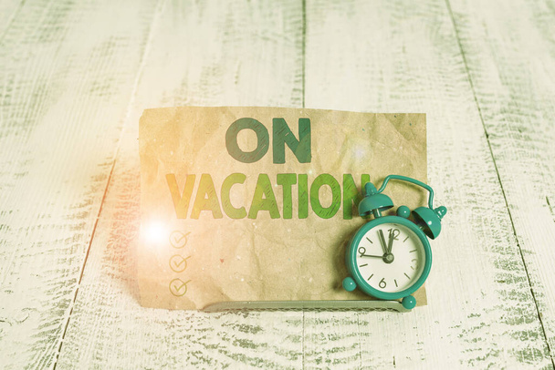 Handwriting text writing On Vacation. Concept meaning period spent away from home or business in travel or recreation Mini blue alarm clock stand tilted above buffer wire in front of notepaper. - 写真・画像
