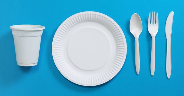 Disposable cutlery on blue background, top view. Glass, plate, spoon, fork, knife - Фото, зображення
