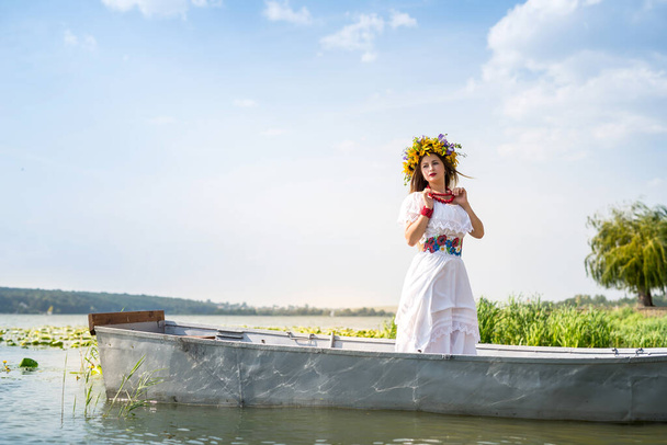 Όμορφο κορίτσι σε εθνικό φόρεμα σε βάρκα στη λίμνη - Φωτογραφία, εικόνα