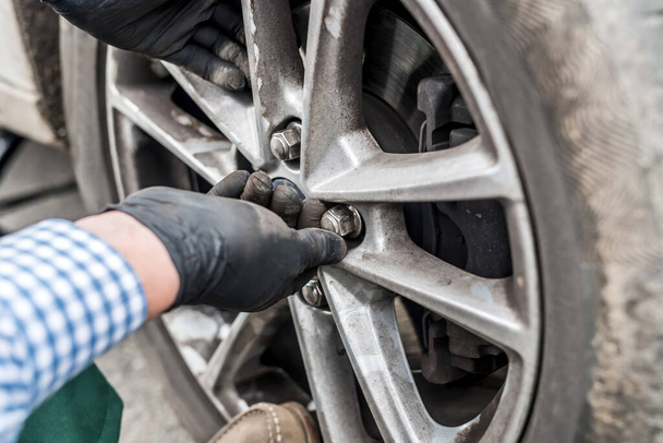 Hands in gloves fixing nuts on car wheel closeup - Photo, Image