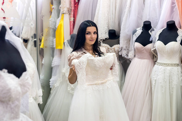 attraktive Verkäuferin im Brautsalon mit Brautkleidern - Foto, Bild