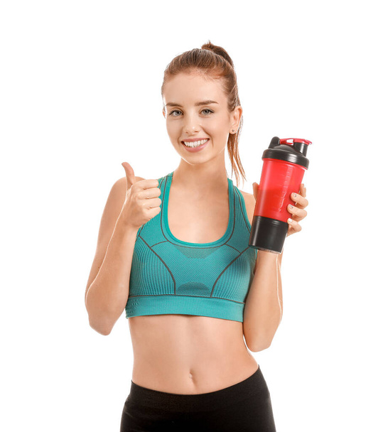 Sportliche junge Frau mit Proteinshake zeigt Daumen nach oben auf weißem Hintergrund - Foto, Bild