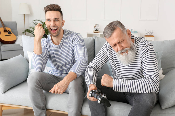 Старший мужчина и его взрослый сын играют в видеоигры дома
 - Фото, изображение