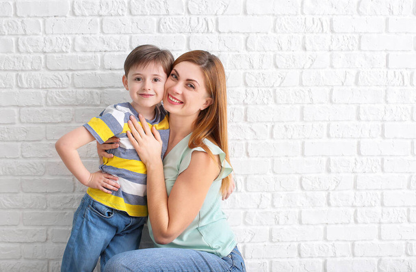 Ευτυχισμένο μικρό αγόρι και η μητέρα του κοντά σε λευκό τοίχο από τούβλα - Φωτογραφία, εικόνα