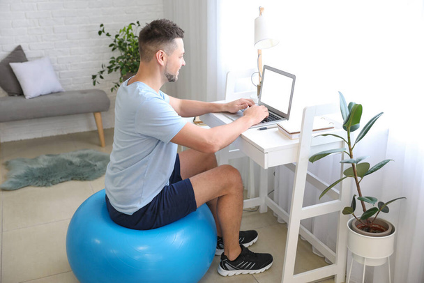 Man sitting on fitness ball while working at home - Photo, Image