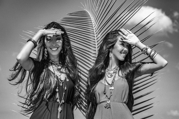two beautiful twin sisters in elegant dresses having fun on tropical beach.  - Foto, Imagen