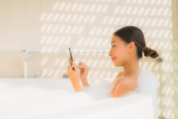 Portret jonge aziatische vrouw met behulp van slimme mobiele telefoon in bad voor spa concept - Foto, afbeelding