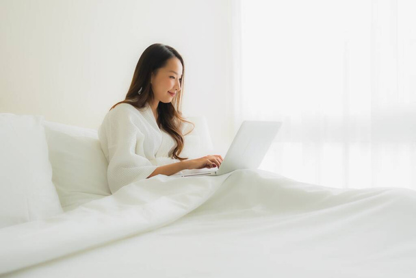 Portrait beautiful young asian women with coffee cup and computer laptop on bed in bedroom interior - 写真・画像