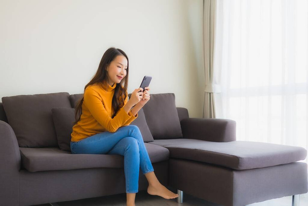 Porträt junge Asiatin mit Smartphone auf Sofa mit Kissen im Wohnzimmer - Foto, Bild