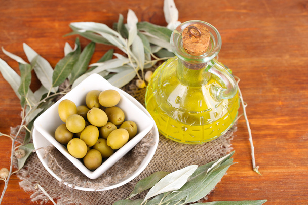 Olives in bowl with branch on sackcloth on wooden table - Фото, зображення