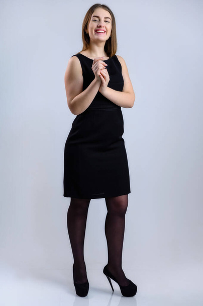 Full length studio photo of a pretty woman with a smile in a black dress on a white background. - Fotó, kép