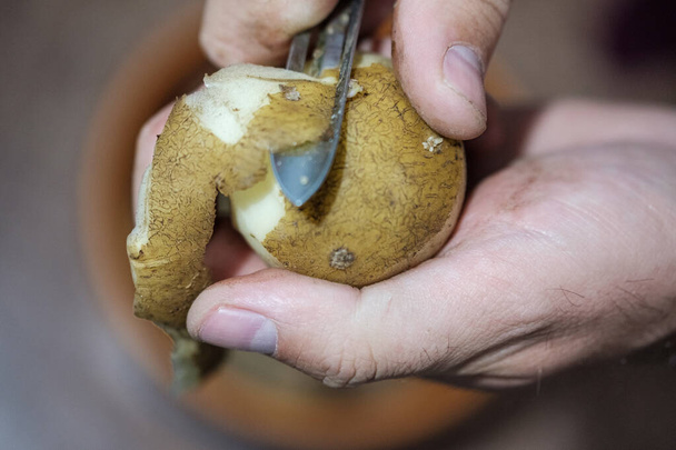 een man schilt aardappelen met een mes speciaal voor het reinigen van groenten - Foto, afbeelding