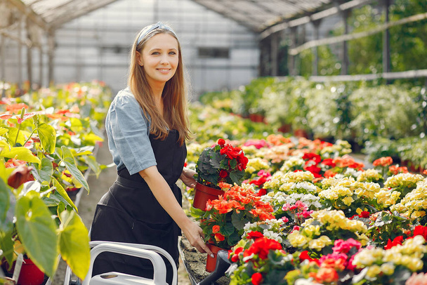 Woman in a black apron working in a greenhouse - Фото, изображение