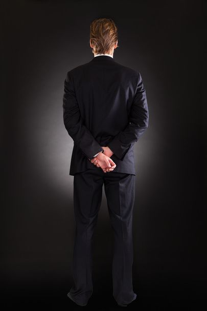 Бизнесмен с руками, стоящими за черным фоном
 - Фото, изображение