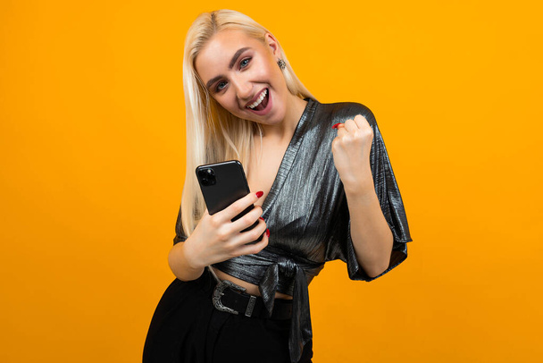 happy charming young woman smiles with joy holding a phone in her hands on a yellow studio background - Photo, image