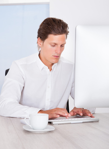 Young Businessman Using Computer With Coffee At Desk - Photo, image