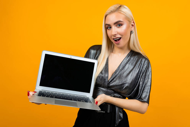 surprised girl holds laptop with template for web page on yellow background - 写真・画像