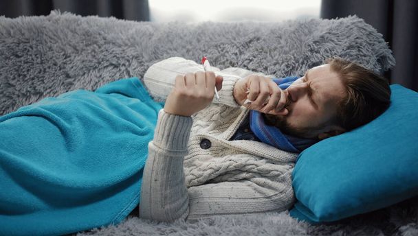 Malato divano uomo cercando termometro
 - Foto, immagini