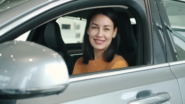 Portrait of girl inside new automobile in car dealership smiling looking at camera - Materiał filmowy, wideo