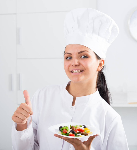 Женщина-повар держит тарелку салата и показывает большие пальцы вверх - Фото, изображение