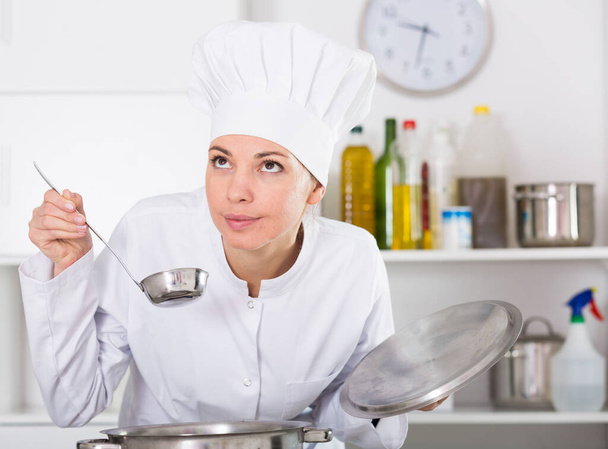 Smiling female cook checking taste of food while preparing in kitchen - Foto, Imagem