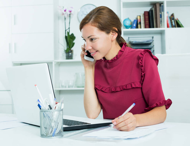 Portrait of confident happy woman working in company office with laptop and talking on phone - Valokuva, kuva