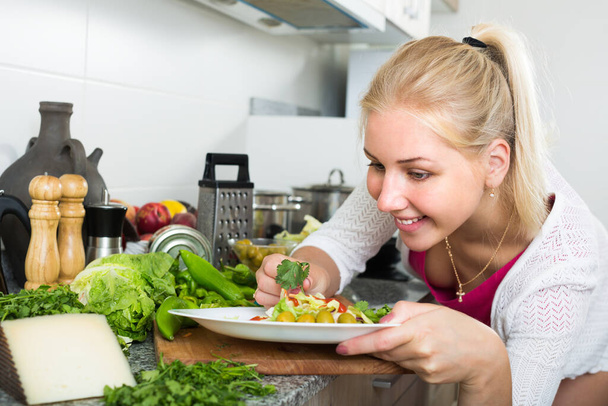 Cheerful young girl preparing healthy green salad on kitchen at hom - Zdjęcie, obraz