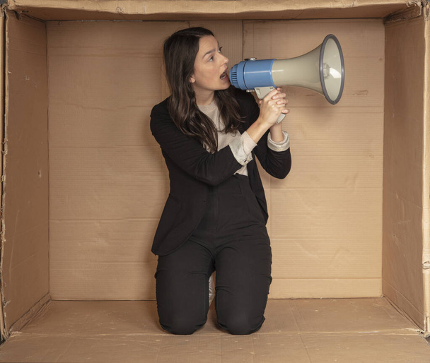 business woman with a megaphone in hand sits in a cramped cardboard office - Photo, Image