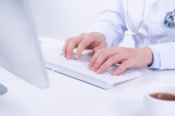 Business concept - Young female doctor woman working at office with computer, typing electronic medical record, white table background, close up, copy space - Photo, Image