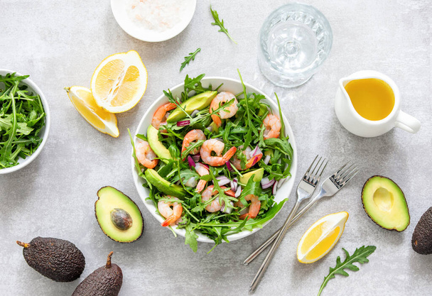 Salada de abacate e salada de arugula de camarões, receita saudável e nutritiva, vista aérea na mesa servida com prato pronto para comer e alguns dos ingredientes.
 - Foto, Imagem